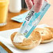A hand holding a Daiya Vegan Cream Cheese single serve packet over a bagel.