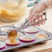 A stainless steel squeeze handle disher being used to portion batter into cupcake liners in a muffin tin.