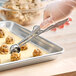 A stainless steel squeeze handle disher being used to portion cookie dough onto a baking sheet.