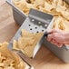 A stainless steel chip scoop with a black handle being used to serve tortilla chips.