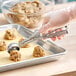 A stainless steel squeeze handle disher being used to portion cookie dough onto a baking sheet.