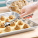 A stainless steel squeeze handle disher being used to portion cookie dough onto a baking sheet.