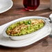A 12 oz. stainless steel oval au gratin dish filled with a baked green casserole and garnished with herbs.