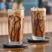 Two glasses of pistachio milk iced coffee on a wooden table.