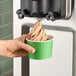 A hand holding a green cup of Turkey Hill chocolate soft serve ice cream.