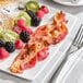 A plate of food with bacon, fruit, and pancakes on a table.