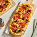 A rectangular Kontos Tavern flatbread topped with pepperoni, cheese, olives, and green herbs, sliced and served on a wooden board.
