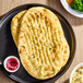 A plate with two pieces of garlic naan bread and a small cup of pickled onions.