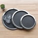 A wooden surface with round black plates and glasses on a non-skid stainless steel tray.
