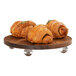 A group of croissants on a Cal-Mil walnut wood round display stand.