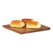 A group of bread rolls on a Cal-Mil walnut wood serving board on a table in a bakery display.