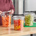 A clear round polycarbonate food storage container with a lid, filled with sliced vegetables.