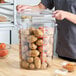 A large clear round polycarbonate food storage container with a lid, filled with potatoes and marked with red measurement lines up to 22 quarts.