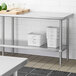 A stainless steel adjustable undershelf installed on a work table in a commercial kitchen setting.