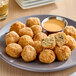 A plate of Jinka Plant-Based Vegan Crab Cake Poppers with a bowl of sauce.