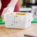 A white square 2-quart polypropylene food storage container with measurement markings and a green lid, partially filled with cut vegetables.