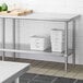 A stainless steel adjustable undershelf installed on a work table, used for additional storage in a kitchen setting.