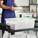 A white polypropylene bus tub or food storage box placed on a utility cart in a commercial kitchen setting.