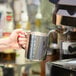 A person using a Service Ideas stainless steel frothing pitcher to pour coffee into a cup.