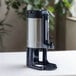 A brushed stainless steel thermal coffee server with a black stand.
