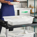 A white polypropylene utility bin holding dishes on a utility cart in a commercial kitchen setting.