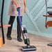 A person using a Dyson WashG1 cordless wet and dry vacuum cleaner on a wooden floor.