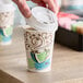 A hand pouring coffee into a Dixie paper cup with a white plastic lid.