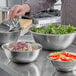 A set of stainless steel mixing bowls in various sizes, some filled with salad and chopped vegetables, on a kitchen counter.