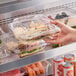 A hand holding a Choice clear hinged plastic container with sandwiches inside.