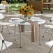 A 48-inch round heavy-duty granite white plastic folding table with gray legs, set for dining and decorated with a vase of sunflowers.