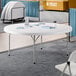 A 72-inch round granite white plastic bi-folding table with gray legs.