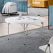 A 60-inch round granite white plastic bi-folding table with gray legs.