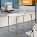 A 24-inch by 48-inch granite white plastic bi-folding table with gray adjustable height legs.