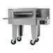 A commercial stainless steel conveyor oven with a wide belt and control panel, mounted on caster wheels.