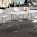A 30 inch by 96 inch granite white plastic bi-folding table with gray legs, set up outdoors with folding chairs.