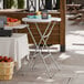 A round, granite white, bar-height plastic folding table with gray legs.