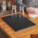 A black Choice bar mat on a wood counter with two glasses on it.