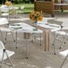 A 60-inch round heavy-duty granite white plastic folding table with gray legs, set outdoors with chairs and table settings.