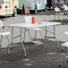 A 30 inch by 60 inch granite white plastic bi-folding table with gray legs, set up outdoors with condiment bottles and napkins on top.