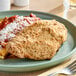 A plate of food with chicken and sauce topped with Imperia Italian-Style Seasoned Bread Crumbs on a wood table.