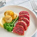 A plate with sliced plant-based vegan lamb, roasted potatoes, broccolini, and a lemon wedge.