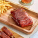 A serving of plant-based vegan bone-in baby ribs with a side of French fries on a wooden tray.