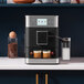 A KitchenAid black espresso machine on a counter with a glass of espresso on top.