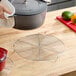 A round, footed stainless steel cooling rack on a wooden countertop.