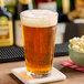 A glass of Hopzoil MAJIK Dank and Stormy beer on a coaster with a bowl of popcorn.