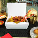 A white Southern Champion take-out box filled with noodles and meatballs with chopsticks on a table.