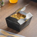 A black Southern Champion paper take-out box filled with rice and vegetables on a table.