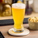 A glass of yellow beer on a coaster.