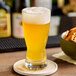 A glass of beer with yellow liquid and foam on a table with a Hopzoil MAJIK&#174; West Coast Fusion&#8482; coaster.