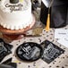 A white square paper napkin with a black graduation cap and yellow tassel on a cake.